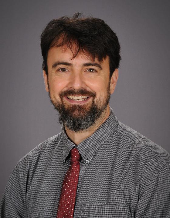 David E Curran smiling in a professional headshot, wearing a grey checked shirt and red tie.